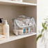 A transparent waterproof cosmetic bag in silver, filled with various skincare products, sits on a shelf.