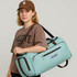 A person wearing a brown cap holds a turquoise convertible backpack duffel garment bag. The bag has a logo.