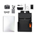 A black flap laptop backpack surrounded by a camera, notebook, glasses, charger, pen, phone, and external drive.