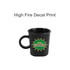 A black ceramic coffee mug with a handle and a colourful graphic featuring the word "GOOD". It has a logo.