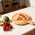 A bamboo wood pizza tray with a slice of pizza, surrounded by strawberries, avocados, and a clean kitchen backdrop.