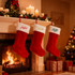 Three red embroidered Christmas stockings with white fur tops hang by a fireplace adorned with candles and a Christmas tree.
