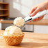 A silver ice cream scoop with a white handle is shown lifting a scoop of ice cream from a waffle cone bowl.