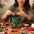 A green drawstring gift bag decorated with Christmas designs, filled with festive ribbons and bows.