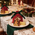 Red ribbon drawstring gift bags on a dining table, with gingerbread cookies and decorative items beside wine glasses.