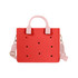 A red tote bag with pink handles and a removable shoulder strap, featuring decorative holes and a logo.