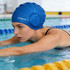 A blue swimming cap with earmuffs is worn by a swimmer in a pool, focusing on her stroke.