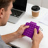 A purple Pop Bubble Board-Square is held by a person at a desk, with a laptop and coffee cup visible.