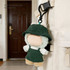 A green plush doll with a hat and overalls, attached to a backpack. Soft and cuddly design.