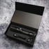 A black rechargeable torch with a charging cable, sitting inside a black box with cushioning.