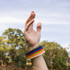 A hand wearing colorful silicone wristbands in blue, red, yellow, green, orange, and white against a natural background.