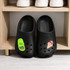 Black clog shoes feature vibrant charms: a green shoe and an ice cream cone. They sit on a shelf beside white sneakers.