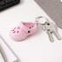 A pink paw shape clog shoe keyring attached to keys, placed on a desk near a notebook and computer.