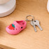 A pink clog shoe keyring with a strawberry design, attached to silver keys on a wooden surface.