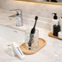 A foldable travel toothbrush in a glass, placed on a wooden tray alongside a bar of soap and bathroom accessories.