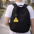 A yellow keychain featuring three bubble buttons hangs from a black backpack. The background includes a path and greenery.