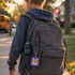 A grey backpack with a blue drink bottle and a purple square fidget keychain hangs from it.