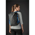 A black backpack with blue accents is worn on the back of a woman in a grey top, set against a dark background.
