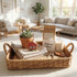 A woven basket holds a plant, folded towels, a candle, a welcome note, keys, and a decorative house piece, all in a sunlit room.