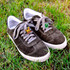 A pair of dark grey sneakers on grass, featuring colourful custom shoelace charms.