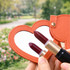 A heart-shaped compact mirror with an orange exterior, featuring a reflective surface and two lipstick shades beside it.