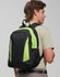 A black and neon green backpack is worn on the back of a young man, featuring mesh pockets and zippers.