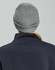 A grey cable knit beanie with a rolled cuff, seen from the back, worn by a person in a navy top.