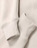 A close-up of a beige oversized hoodie featuring ribbed cuffs and a soft fleece texture. It has a logo.