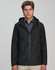 A unisex waterproof jacket in black, featuring a hood and front zipper, modelled by a young man. It has a logo on the sleeve.