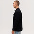 A man models a black Studio Canvas Jacket from the side, featuring a collared design and two front pockets.