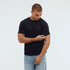 A man wearing a navy blue Essential/Surf Tee and light blue jeans, looking at his sleeve. The image features a logo.