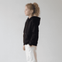 A black youth hoodie with a kangaroo pocket, drawstring hood, and a logo, paired with white trousers.