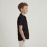 A black polo shirt for youth displayed on a model, featuring a classic design and a logo on the chest.