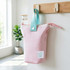 A foldable pink pencil case with a light blue handle, featuring a logo, hanging from a wall hook.