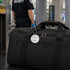 A black luggage bag with a round wire cable luggage tag, placed on a table near security personnel.