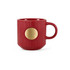 A red ceramic mug with a ribbed design and a bronze medal emblem on the side. It has a curved handle.