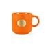 An orange ceramic mug with a textured surface and a bronze medal accent. Features a single handle and a round base.