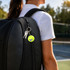 A yellow tennis ball keyring attached to a black backpack, hanging alongside a set of keys.