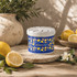 A blue fragrance pot with a lemon pattern, surrounded by fresh lemons and greenery on a textured surface.