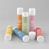 A collection of flavoured lip balms in pastel shades of pink, green, orange, yellow, and white, featuring a logo.