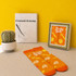 A framed picture in a decorative frame, with orange-patterned socks displayed beside a cactus and a drawing book.