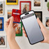 A hand holds a red NFC acrylic fridge magnet next to a smartphone. Various colourful magnets adorn a wall.