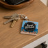 A NFC acrylic spinning keychain featuring a vinyl record design, alongside several keys on a wooden surface.