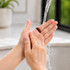 A dark ceramic ring is held between two hands under running water, with a blurred background.