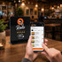 A black NFC acrylic menu stand with a logo, next to a person using a smartphone to view a menu.