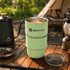 A double wall stainless steel round bottom camping mug in mint green with a lid, featuring a logo.