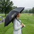 A black umbrella with a logo, held by a person on a golf course during rainy weather.