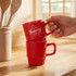 Two red stackable coffee mugs, one being held and the other resting underneath, on a wooden kitchen countertop.