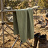 A green Frontier Rapid Dry Towel hangs from a camping chair beside a fire, with boots on the ground nearby.