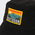 A black terry towelling bucket hat featuring a full colour patch depicting mountains and a sunset.